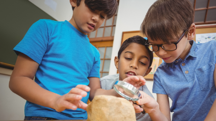 3 kids looking at a rock through a magnifying glass